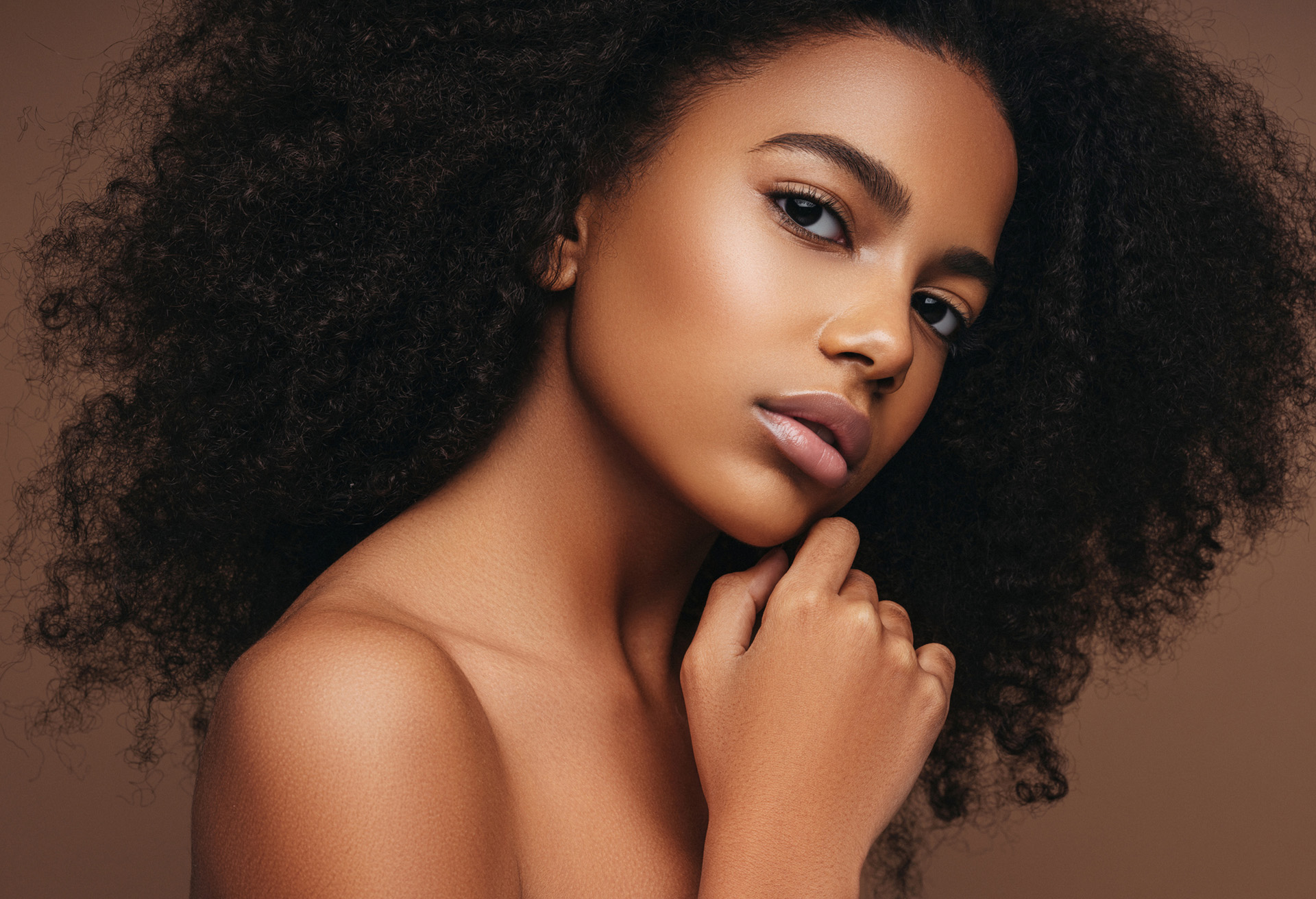 Woman with very curly hair with hand on chin